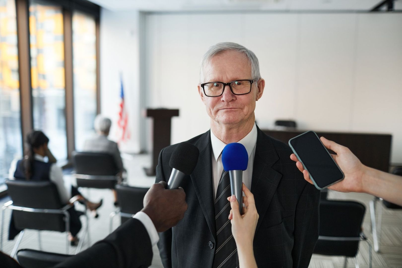 Politiker im Anzug wird von Medien mit Mikrofonen und Smartphone befragt